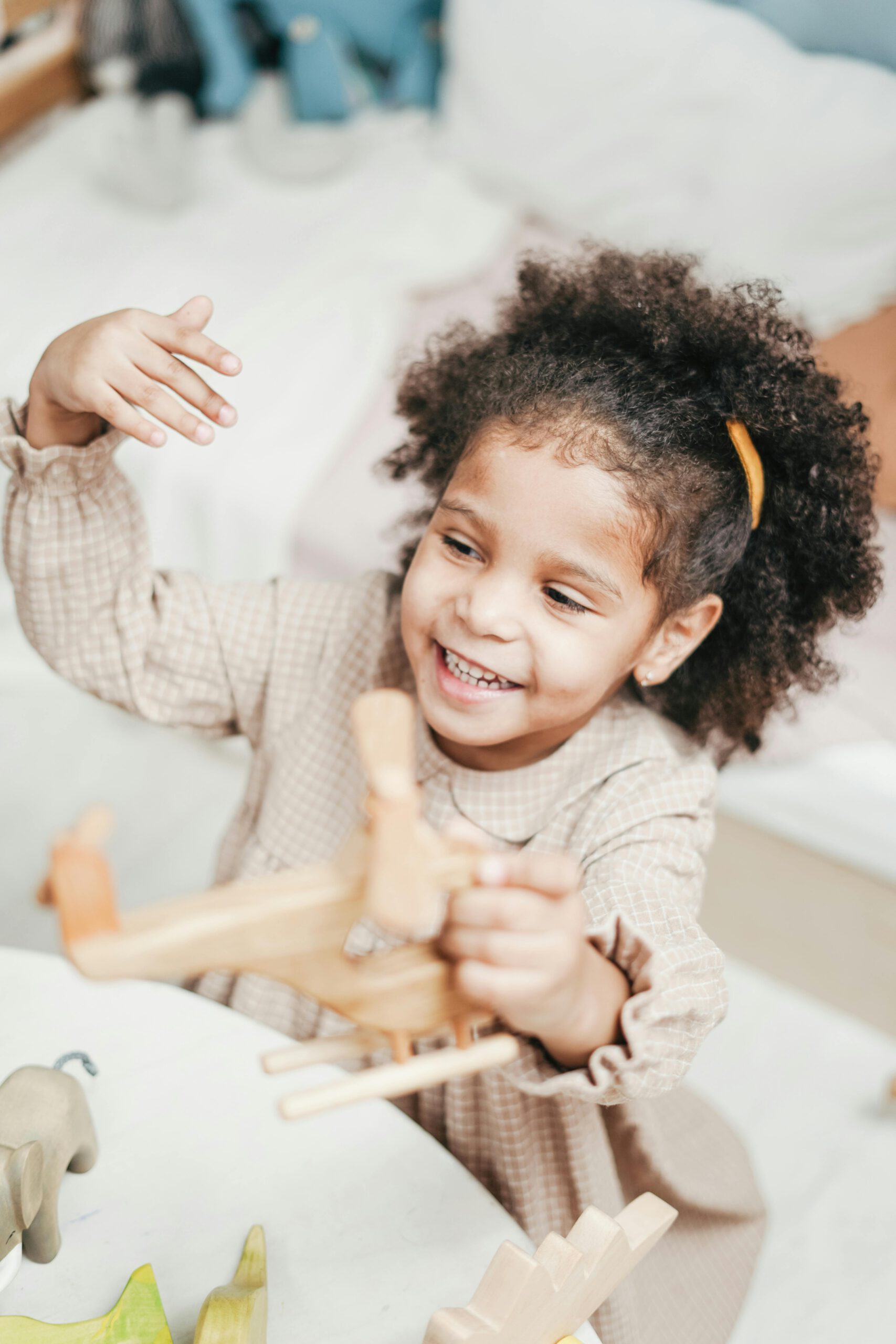 A happy girl with afro hair enjoying playtime with wooden toys in a cozy room.